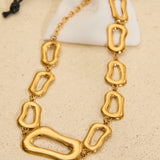 Gold stainless steel statement necklace featuring polished organic-shaped links displayed on a neutral background with a white jewellery pouch.