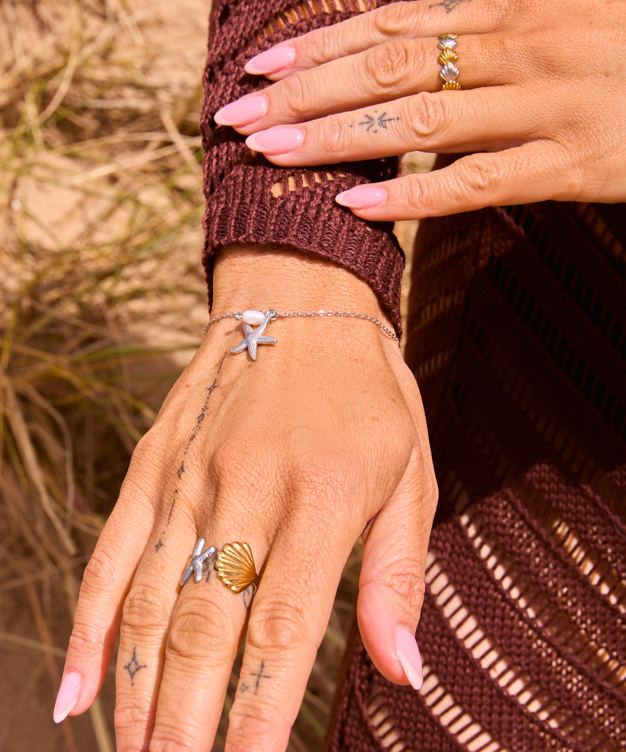 Silver dainty chain bracelet with a freshwater pearl bead and silver starfish charm pendant, displayed on a The Seventh Edit pouch in sand.​​​​​​​​​​​​​​​​Uk jewellery 