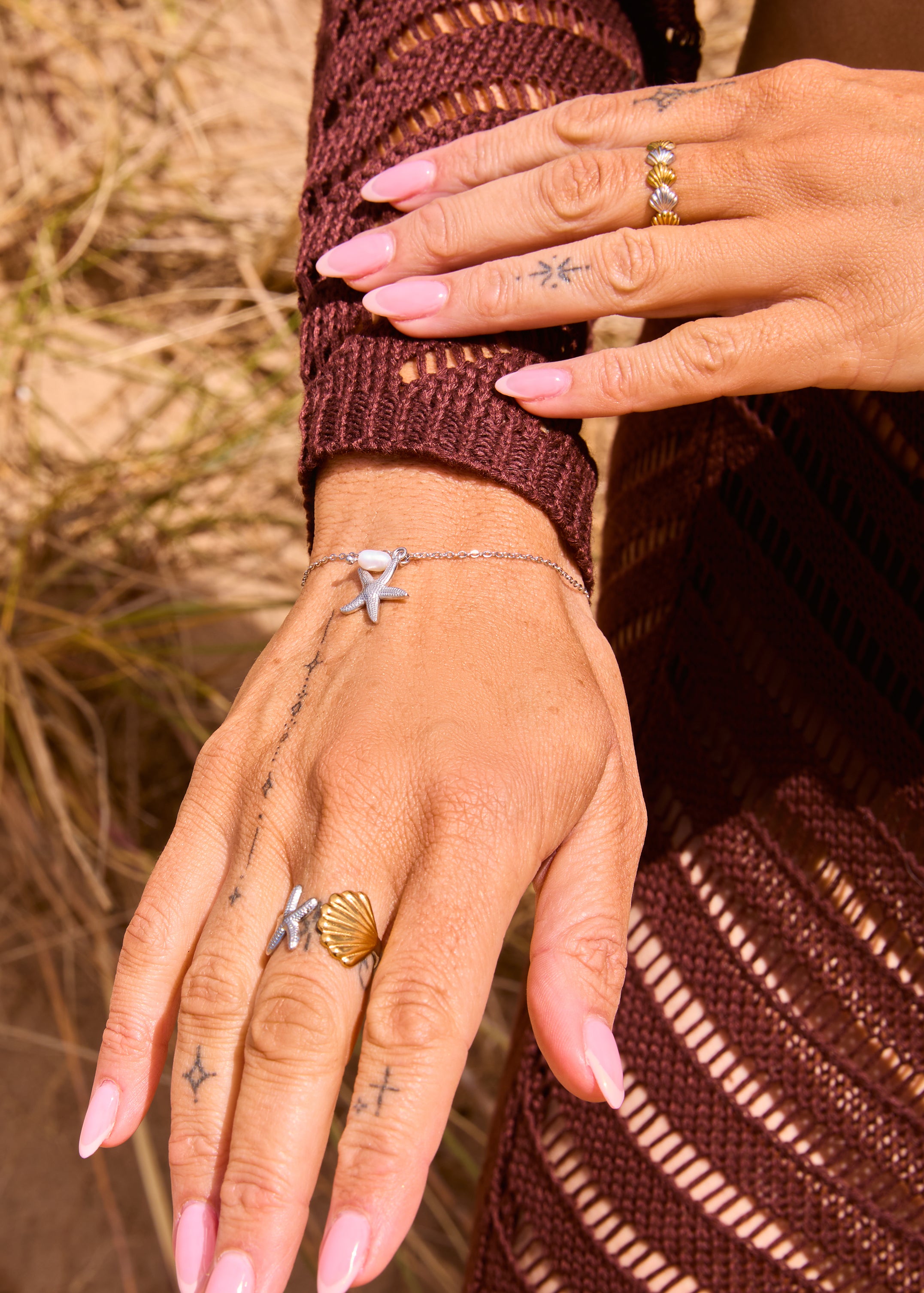 Silver dainty chain bracelet with a freshwater pearl bead and silver starfish charm pendant, displayed on a The Seventh Edit pouch in sand.​​​​​​​​​​​​​​​​Uk jewellery 