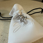 The Frankie Hoops,triple-band open hoop earrings, laid on The Seventh Edit’s branded white pouch.