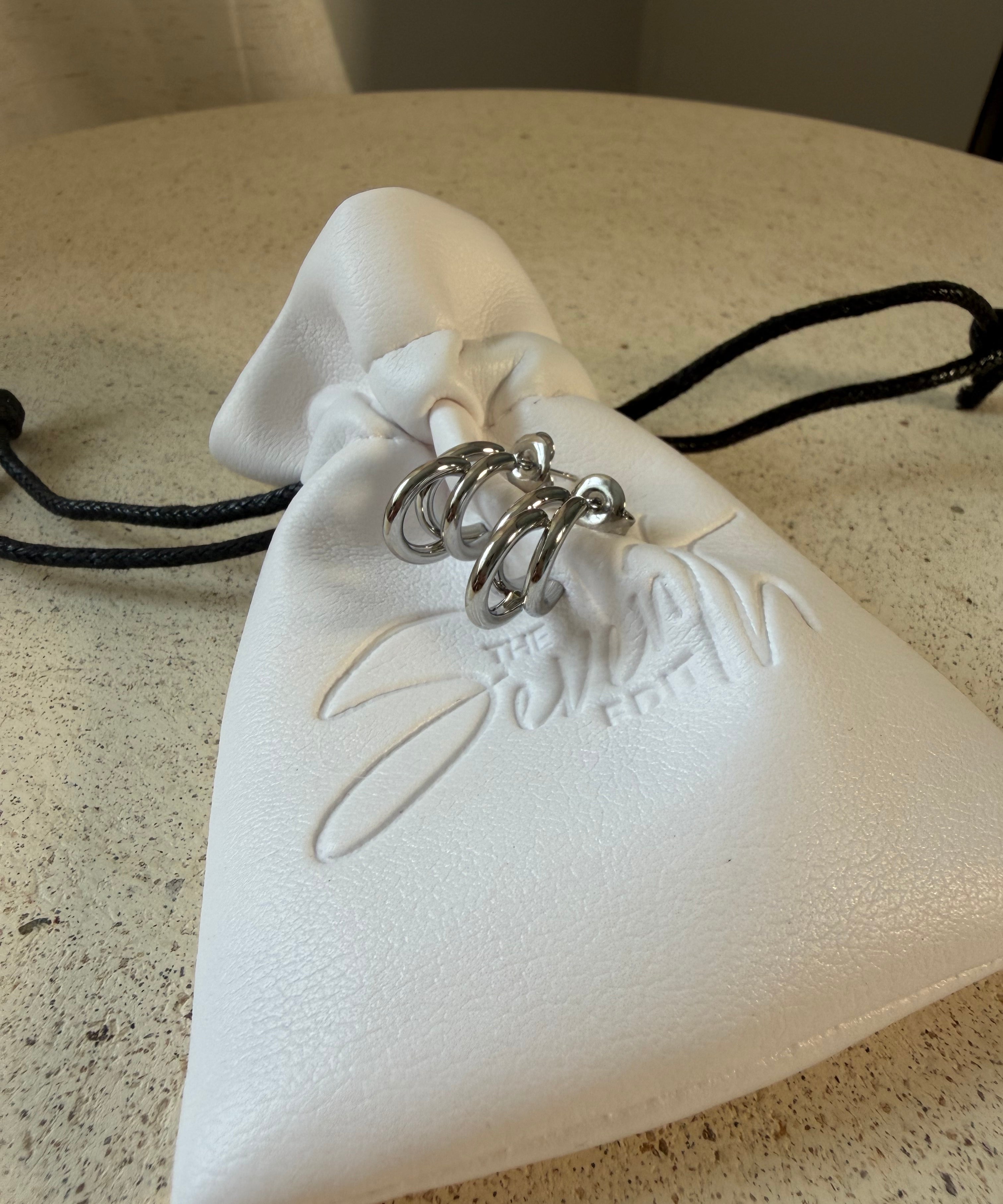 The Frankie Hoops,triple-band open hoop earrings, laid on The Seventh Edit’s branded white pouch.