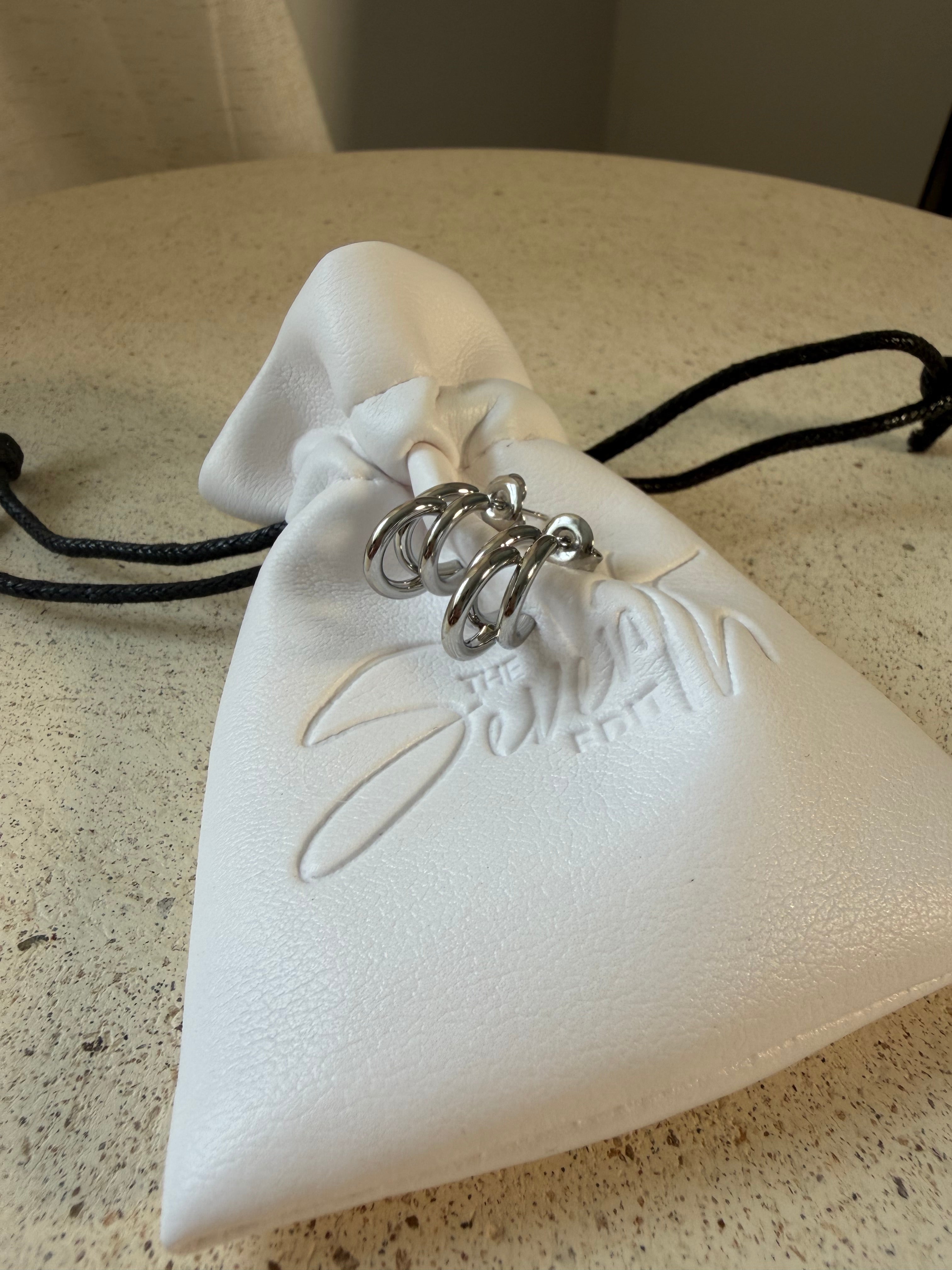 The Frankie Hoops,triple-band open hoop earrings, laid on The Seventh Edit’s branded white pouch.