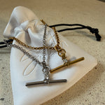 The Sadie Necklace, a waterproof gold belcher chain necklace with pavé T-bar pendant, laid on The Seventh Edit’s branded white pouch.