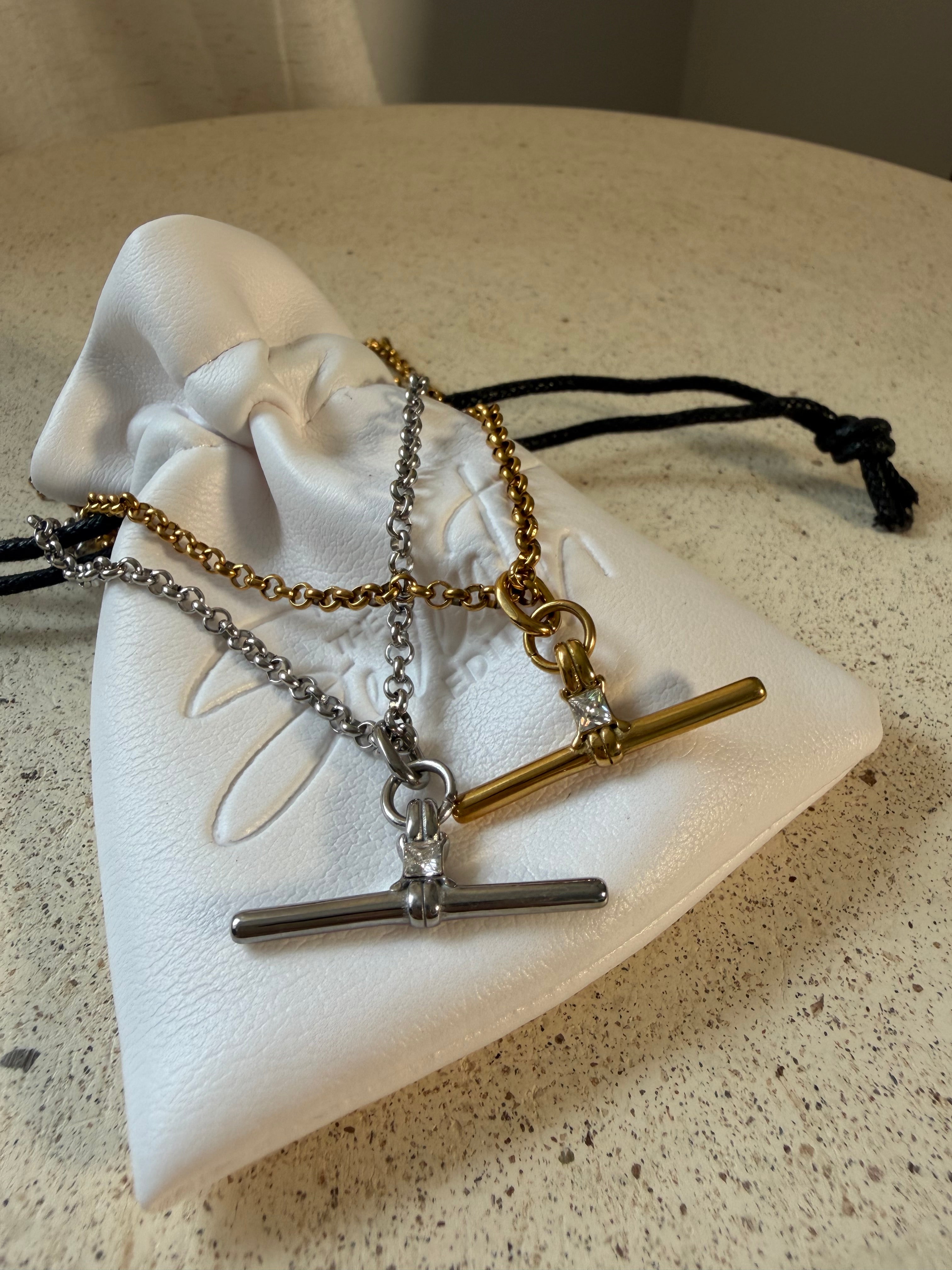 The Sadie Necklace, a waterproof gold belcher chain necklace with pavé T-bar pendant, laid on The Seventh Edit’s branded white pouch.
