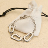 Silver stainless steel organic link bracelet with polished abstract links displayed on a white jewellery pouch.