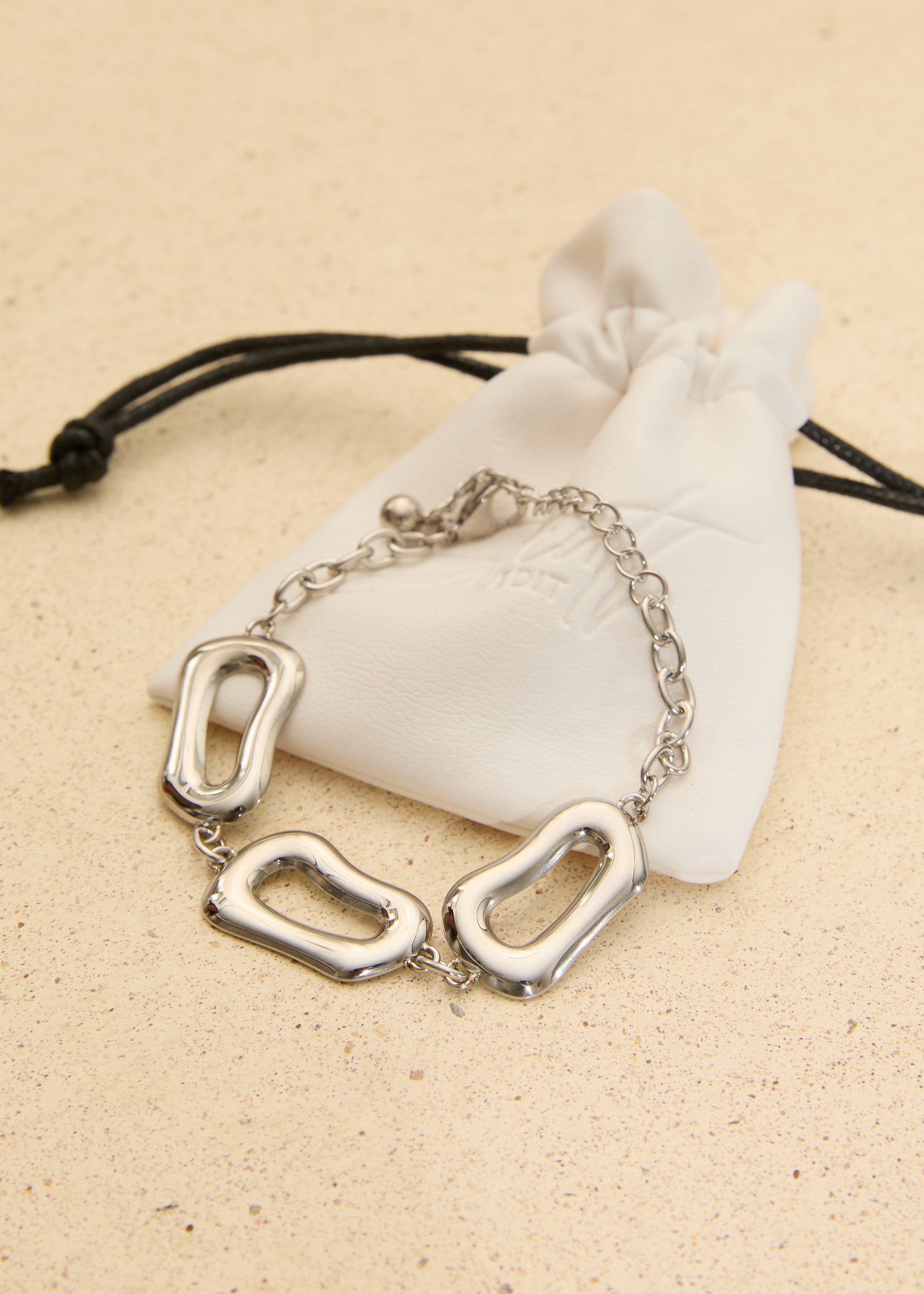 Silver stainless steel organic link bracelet with polished abstract links displayed on a white jewellery pouch.