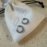 The Rio Hoops, silver twisted rope huggie hoop earrings, laid on The Seventh Edit’s branded white pouch.