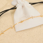 The Seventh Edit Stella Bracelet — gold crystal star charm chain bracelet draped across a white branded pouch on sand.