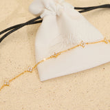 The Seventh Edit Stella Bracelet — gold crystal star charm chain bracelet draped across a white branded pouch on sand.