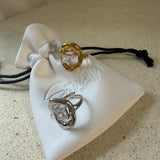 The Delphine Ring, a gold sculptural open ring with princess-cut stone, laid on The Seventh Edit’s branded white pouch.